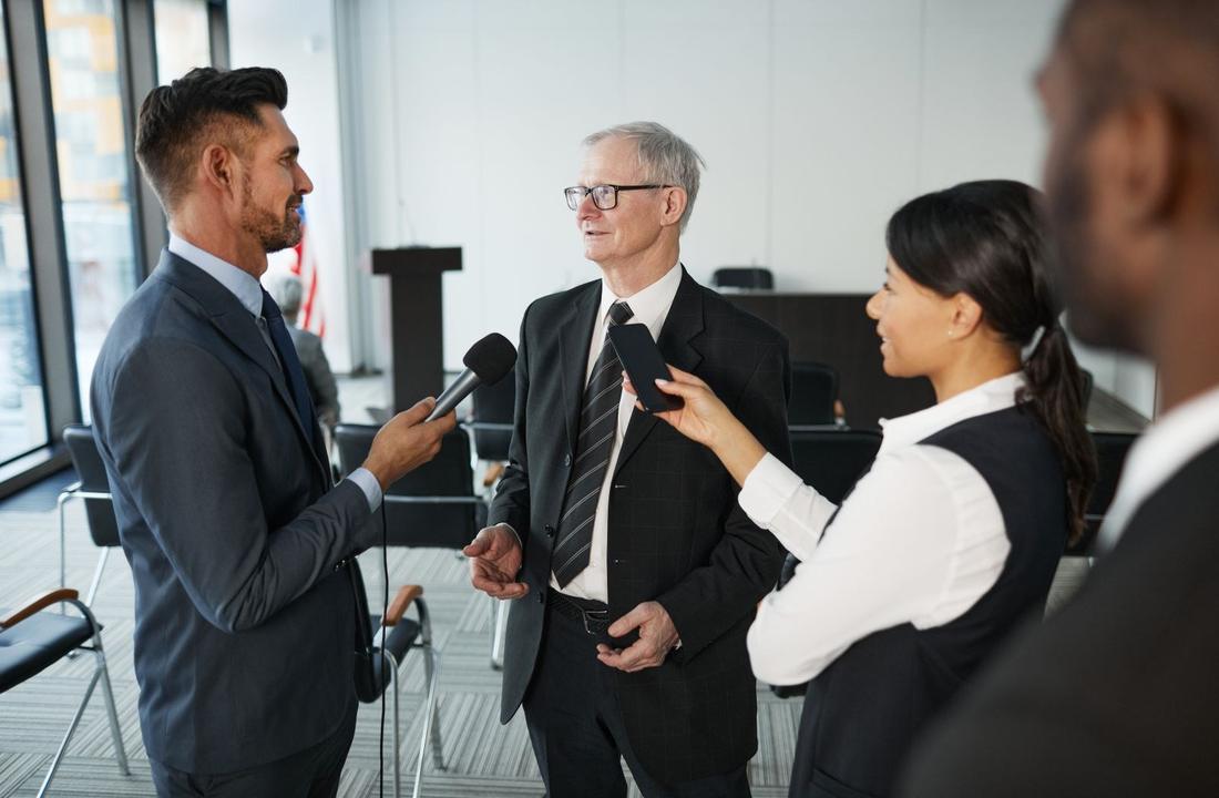 An executive speaking to journalists with advisers beside him
