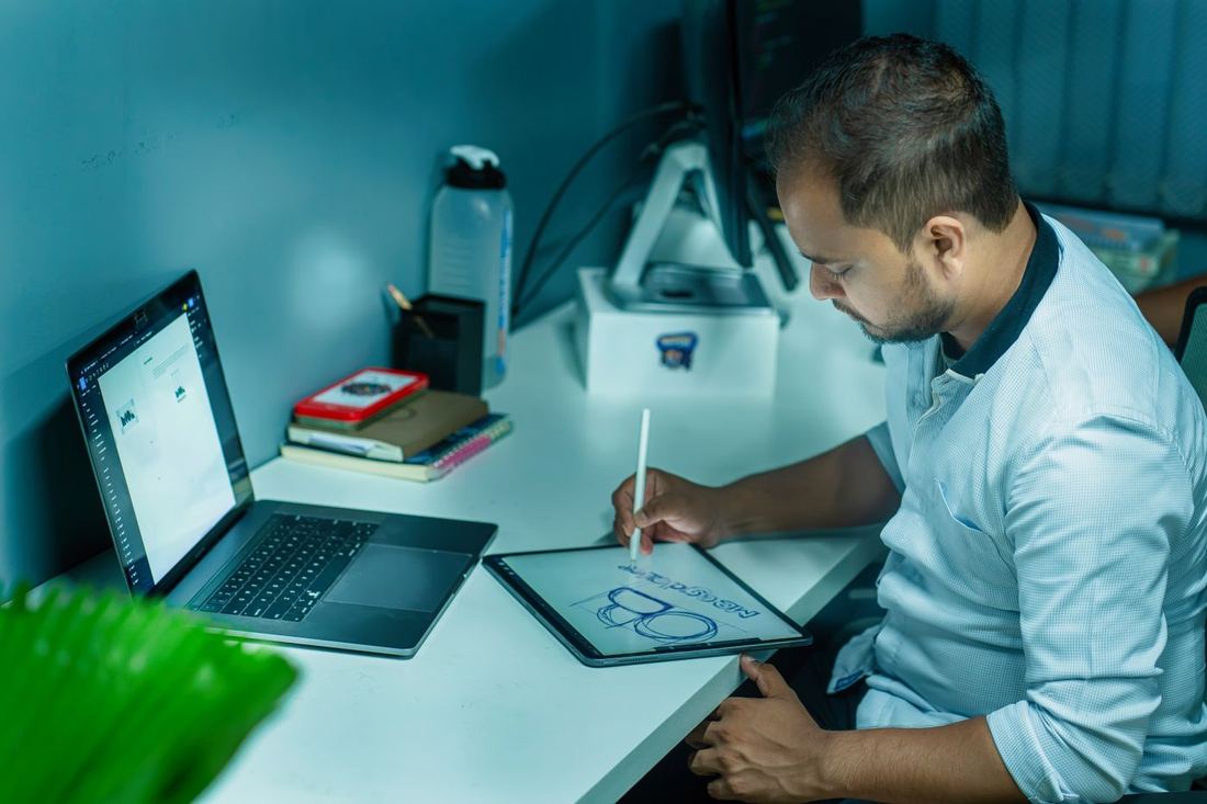 Dizüstü bilgisayarın yanında grafik tablete çizim yapan bir adam