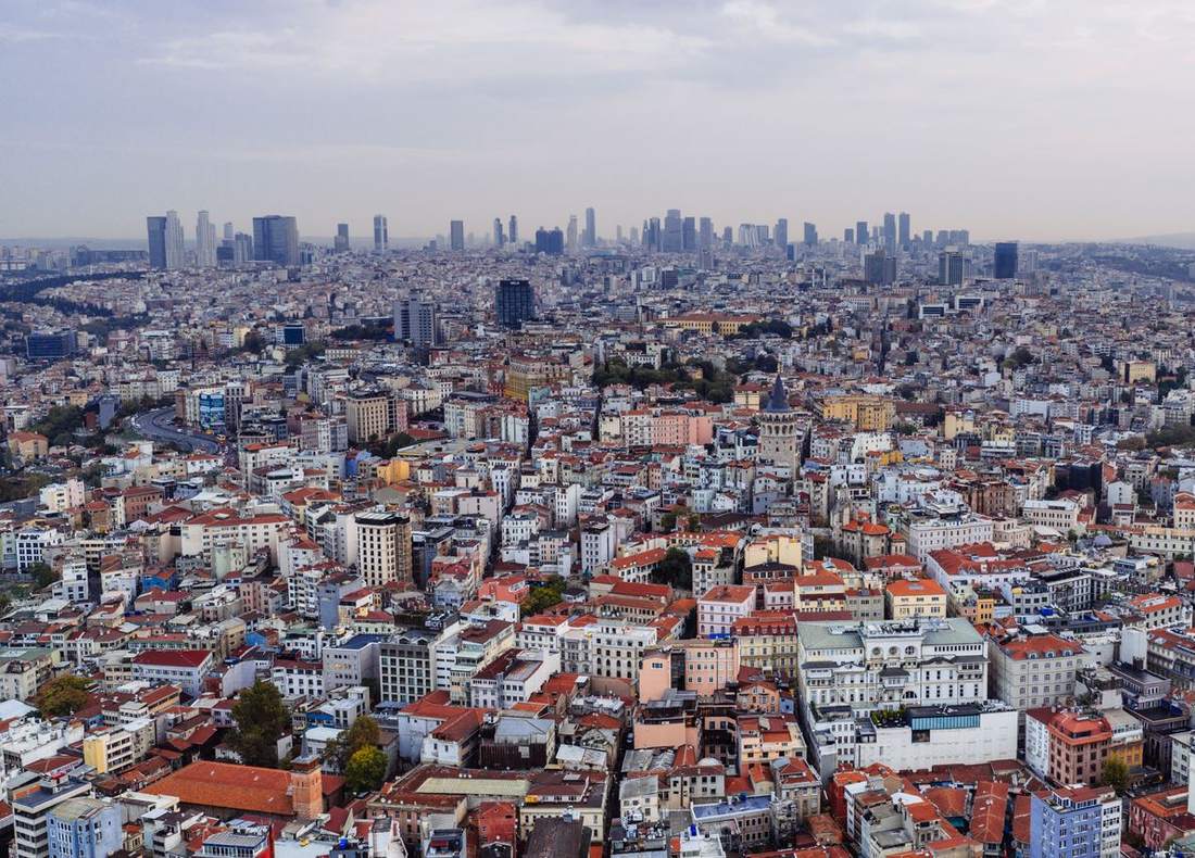 Havadan çekilmiş, kiremit çatılı eski doku ve ufukta gökdelenlerle bir kent