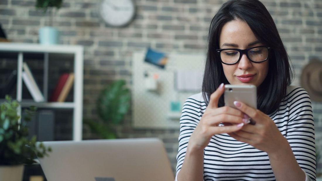 Ofiste akıllı telefonuna bakan gözlüklü bir kadın